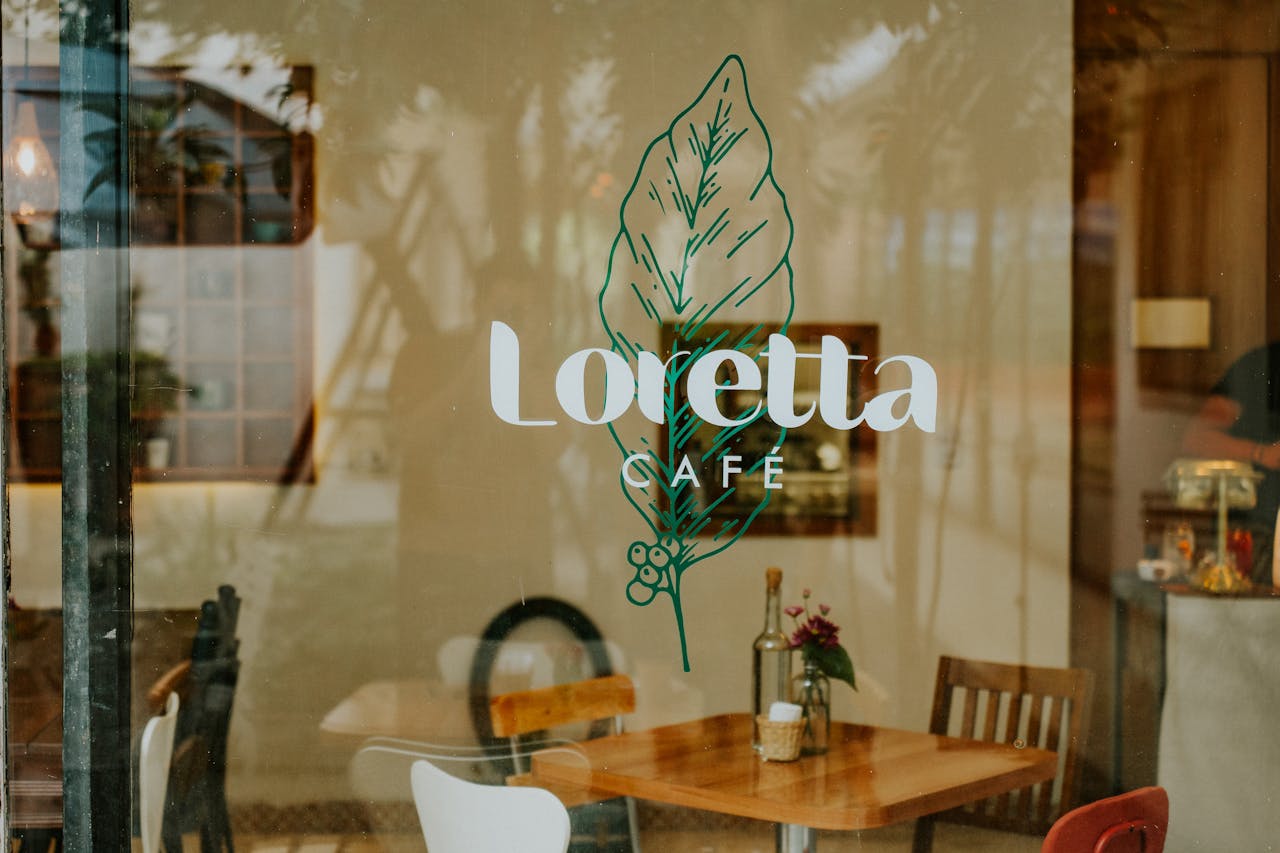 A warm look inside Loretta Café, showcasing rustic furniture through a glass window.